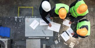 Overhead view of construction workers looking at drawings on a table.