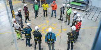 Construction workers with harnesses standing in a circle while being briefed.